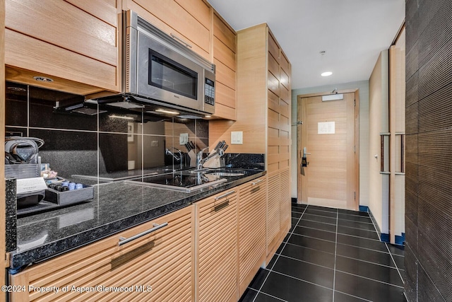 kitchen with backsplash, dark stone counters, black electric cooktop, dark tile patterned floors, and light brown cabinets