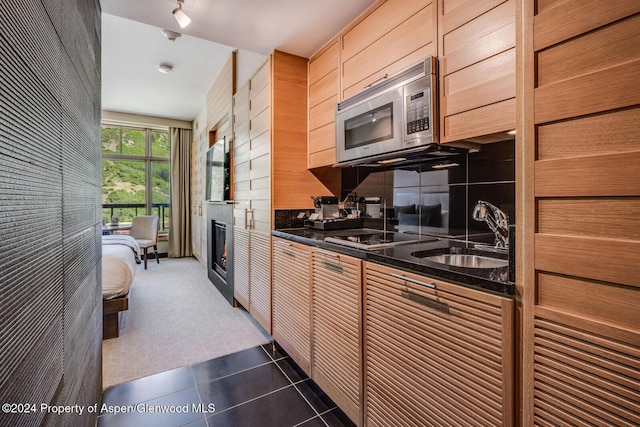 kitchen featuring decorative backsplash, black electric stovetop, dark tile patterned floors, wooden walls, and sink