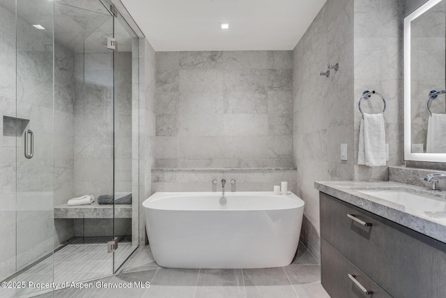 full bath featuring a shower stall, a freestanding bath, vanity, and tile walls