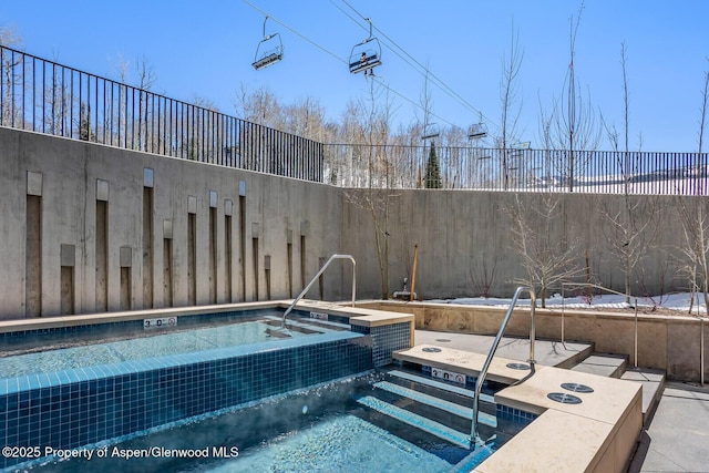 view of swimming pool featuring fence and a hot tub