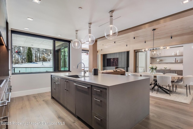 kitchen featuring modern cabinets, light wood-type flooring, a sink, hanging light fixtures, and a center island with sink