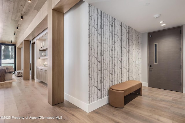 hallway with wood finished floors, an accent wall, and baseboards