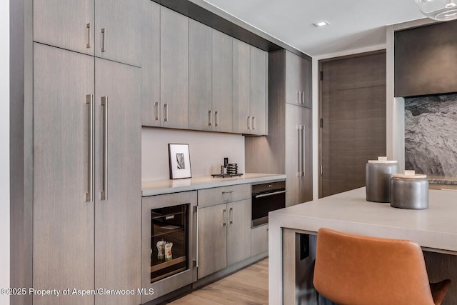 kitchen with built in refrigerator, light countertops, light wood-type flooring, black oven, and beverage cooler