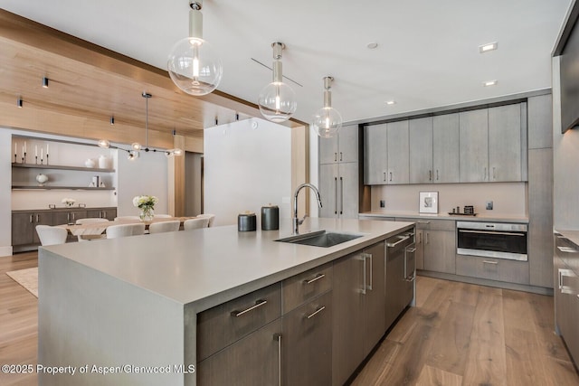 kitchen with an island with sink, light wood-style flooring, light countertops, a sink, and oven