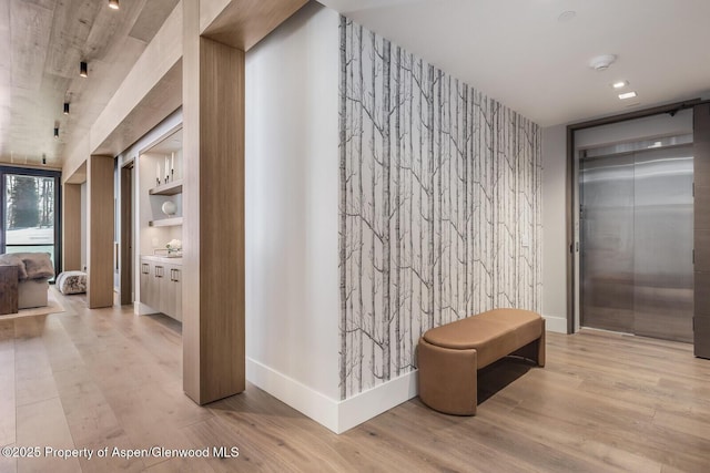 hallway featuring rail lighting, an accent wall, baseboards, and wood finished floors