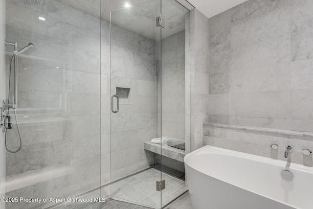 bathroom with a shower stall, a freestanding tub, and tile walls