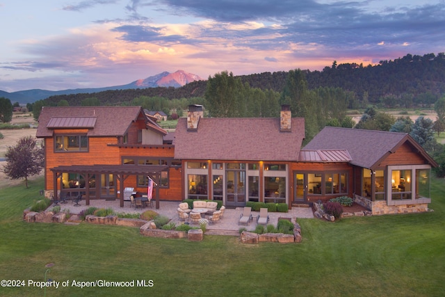 back house at dusk featuring a pergola, outdoor lounge area, a patio area, a mountain view, and a yard