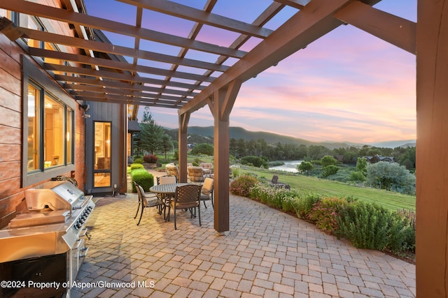 patio terrace at dusk featuring a pergola, area for grilling, and a water view