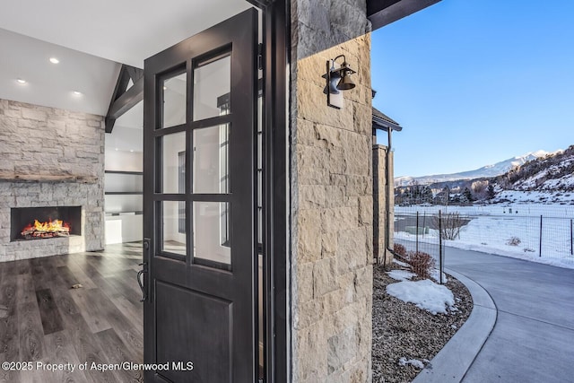 snow covered property entrance featuring a mountain view and an outdoor stone fireplace