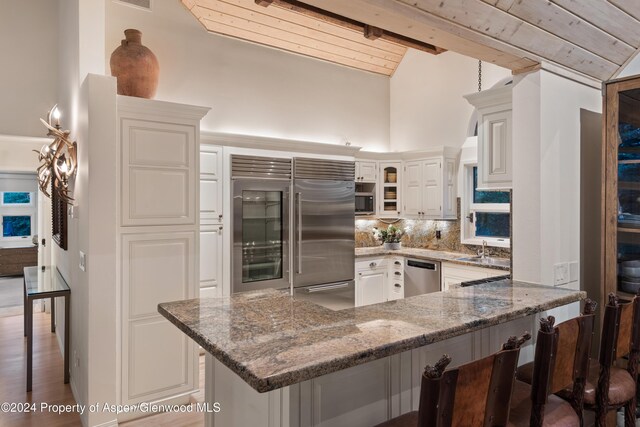 kitchen featuring a breakfast bar, appliances with stainless steel finishes, tasteful backsplash, light stone counters, and white cabinetry