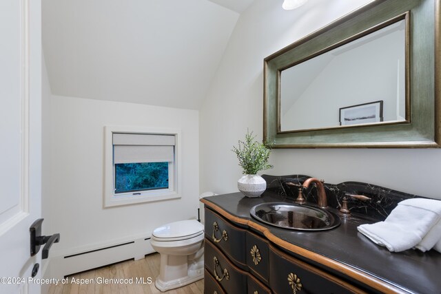 bathroom featuring vanity, a baseboard heating unit, wood-type flooring, toilet, and lofted ceiling