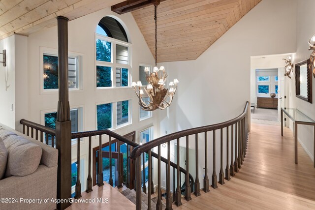 stairway with an inviting chandelier, high vaulted ceiling, beamed ceiling, hardwood / wood-style floors, and wood ceiling