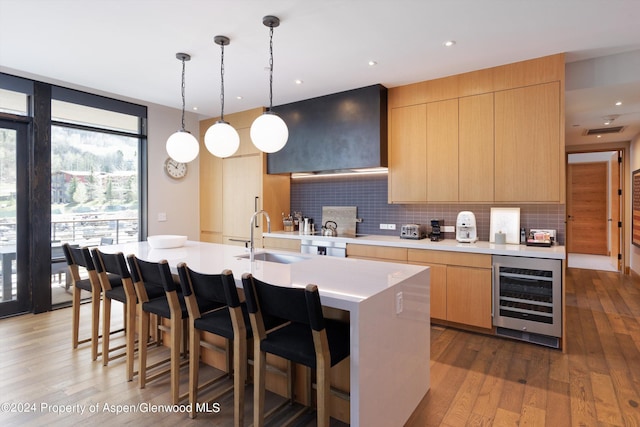 kitchen with wine cooler, sink, light brown cabinets, pendant lighting, and a kitchen island with sink