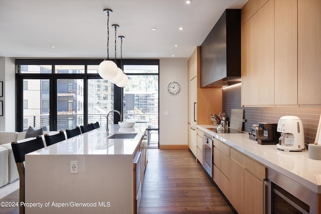 kitchen with wall chimney range hood, a kitchen island with sink, tasteful backsplash, beverage cooler, and light brown cabinets