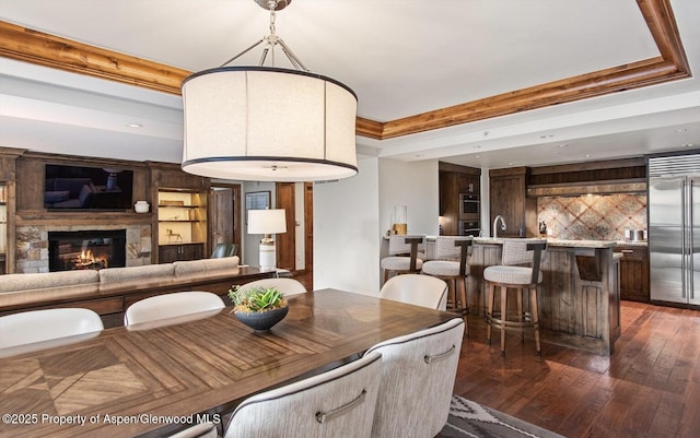 dining space with built in shelves, a raised ceiling, sink, dark hardwood / wood-style floors, and a stone fireplace