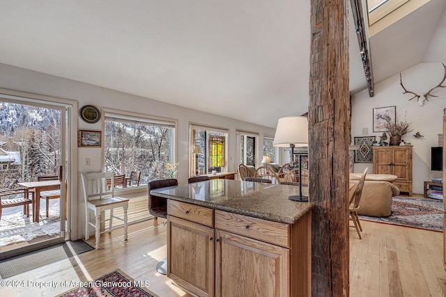 kitchen with light wood-type flooring, lofted ceiling with beams, and dark stone counters