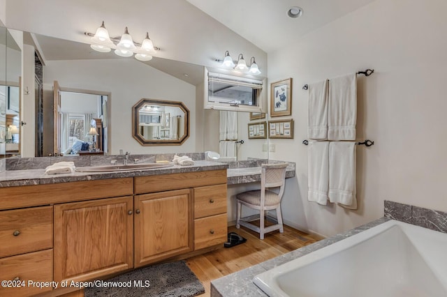 bathroom with a bath, hardwood / wood-style floors, and vaulted ceiling