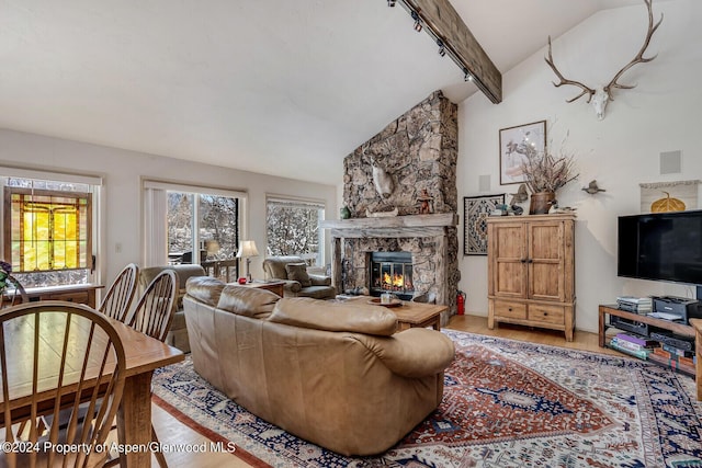 living room with a stone fireplace, hardwood / wood-style floors, rail lighting, and vaulted ceiling