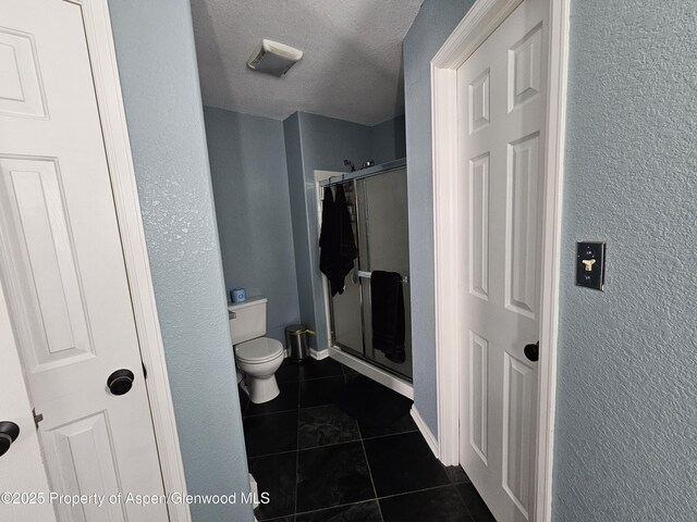 1650 Dogwood Dr, Rifle, CO 81650 - bathroom with tile patterned floors, a stall shower, toilet, a textured wall, and a textured ceiling
