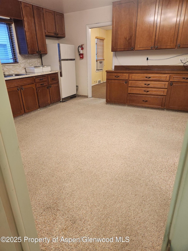 kitchen featuring freestanding refrigerator, a sink, decorative backsplash, cooling unit, and brown cabinetry