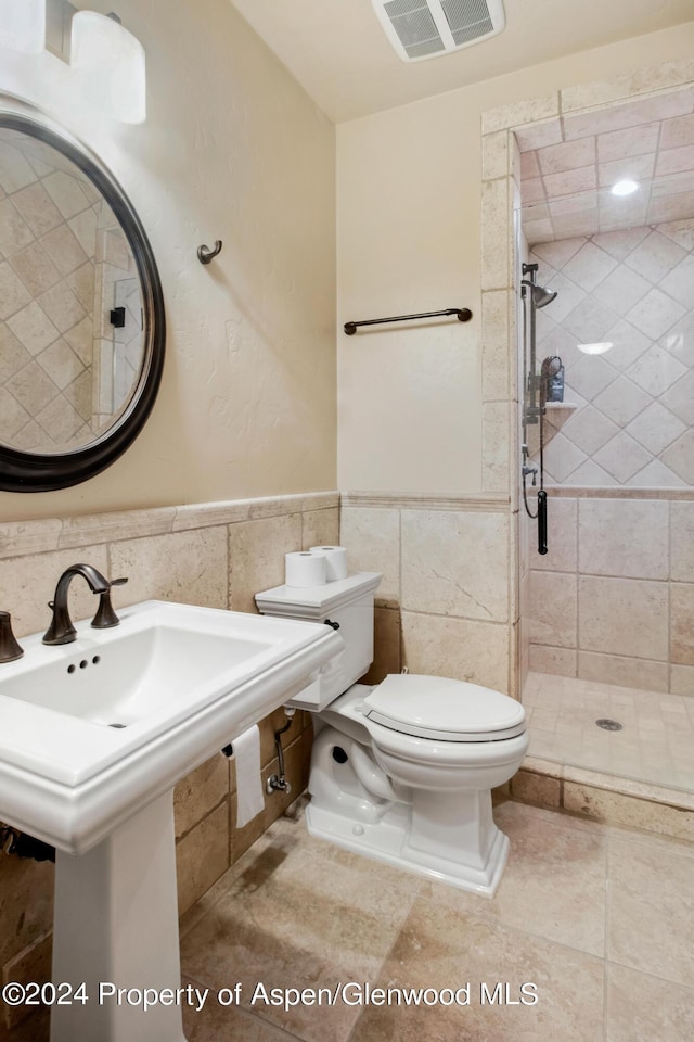 bathroom with a tile shower, toilet, and tile walls