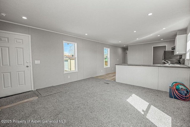 unfurnished living room featuring recessed lighting, carpet, a sink, and crown molding