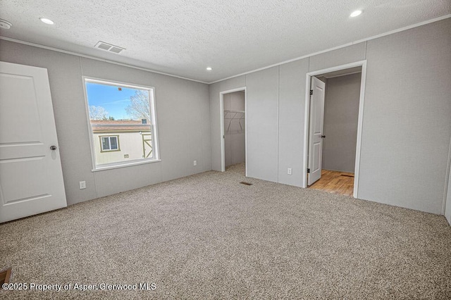 unfurnished bedroom featuring ornamental molding, carpet flooring, a textured ceiling, a walk in closet, and visible vents