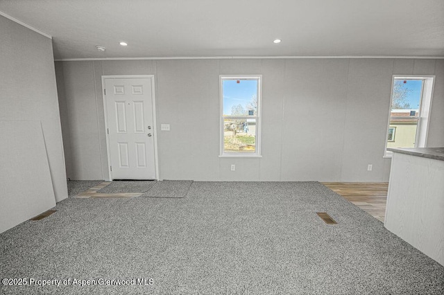 unfurnished living room featuring a wealth of natural light, ornamental molding, and carpet floors