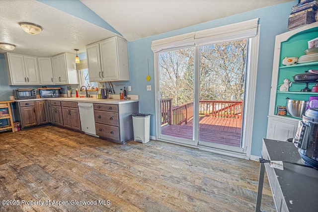 kitchen with dishwasher, a sink, light countertops, dark wood-style floors, and vaulted ceiling