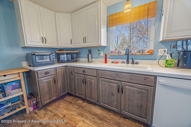 kitchen with dark wood finished floors, white cabinetry, dishwasher, light countertops, and a sink