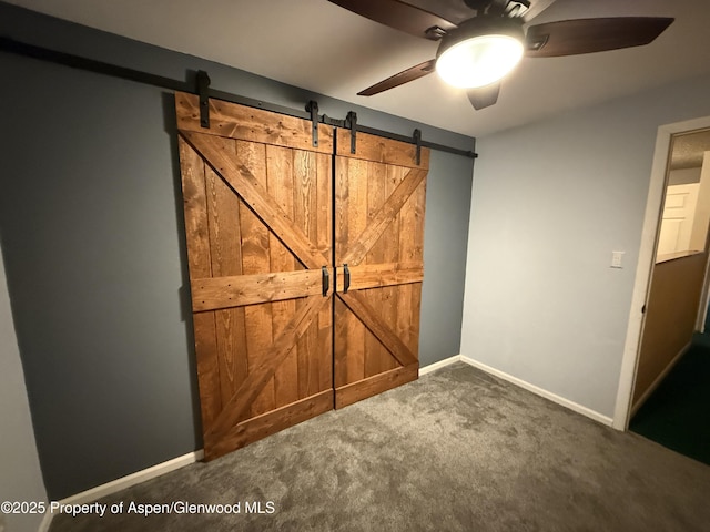 unfurnished bedroom with carpet floors, baseboards, ceiling fan, and a barn door