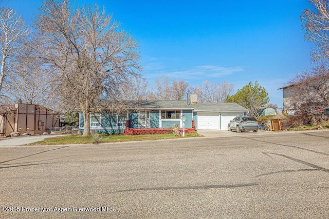 single story home with concrete driveway, a chimney, and an attached garage