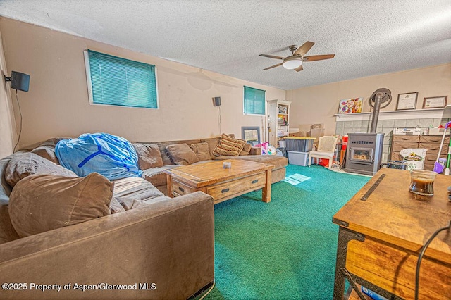 carpeted living room featuring a wood stove, ceiling fan, and a textured ceiling