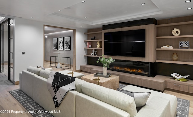 living room featuring a raised ceiling, built in shelves, and light hardwood / wood-style floors