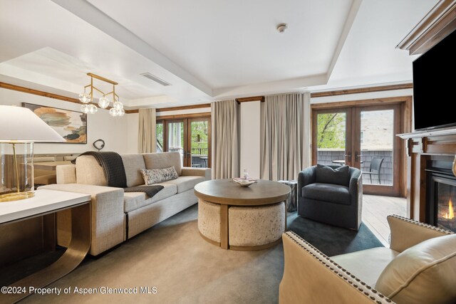 living room featuring carpet flooring, an inviting chandelier, a raised ceiling, and french doors