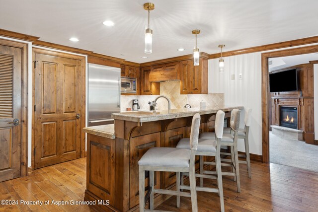 kitchen featuring light stone countertops, built in appliances, light hardwood / wood-style floors, decorative light fixtures, and decorative backsplash