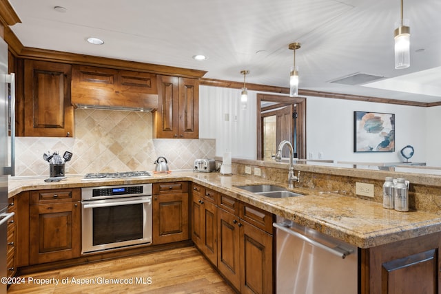 kitchen with backsplash, stainless steel appliances, sink, pendant lighting, and light hardwood / wood-style flooring