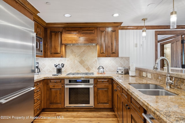 kitchen with light stone countertops, sink, light hardwood / wood-style flooring, decorative light fixtures, and appliances with stainless steel finishes