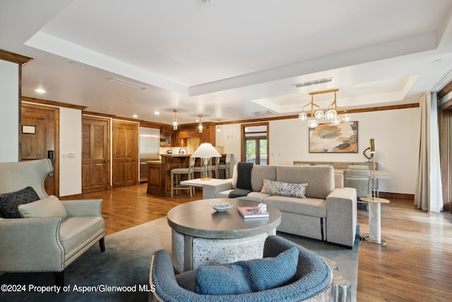 living room featuring a tray ceiling, light hardwood / wood-style flooring, and a notable chandelier