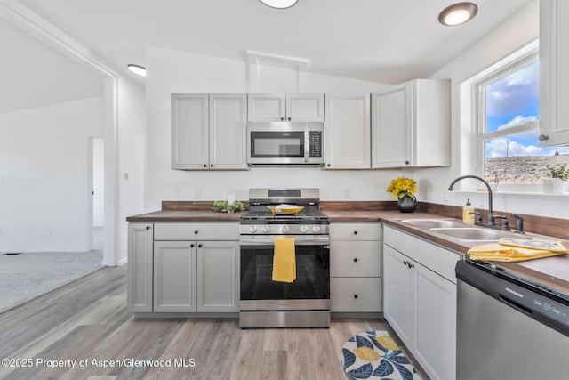 kitchen with lofted ceiling, stainless steel appliances, a sink, and light wood-type flooring