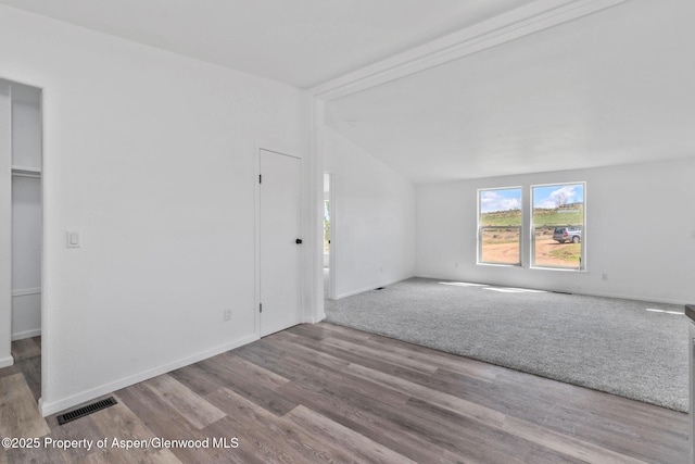 spare room featuring wood finished floors, baseboards, vaulted ceiling, and visible vents