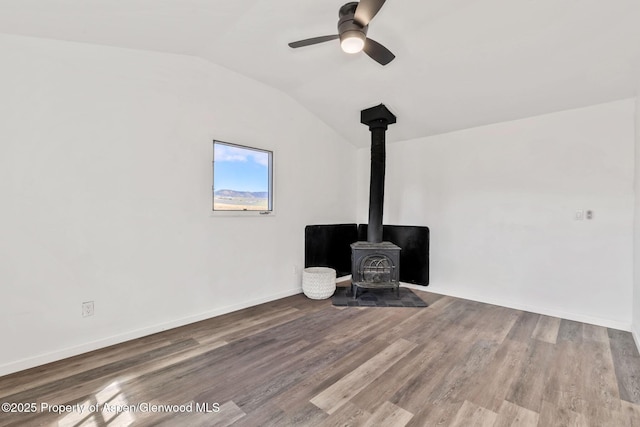 room details with wood finished floors, a wood stove, a ceiling fan, and baseboards