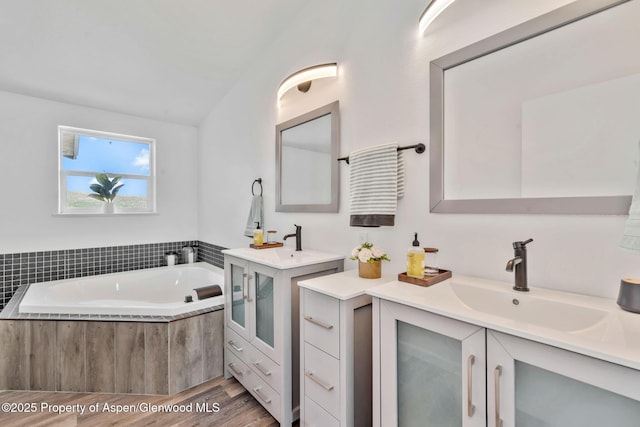 full bath featuring two vanities, wood finished floors, a garden tub, and a sink