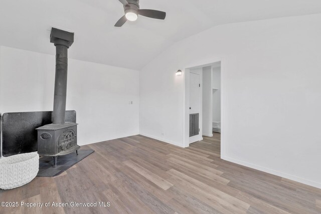 unfurnished living room featuring a ceiling fan, wood finished floors, vaulted ceiling, and a wood stove