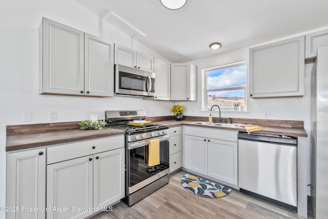 kitchen featuring a sink, wooden counters, light wood-style floors, lofted ceiling, and appliances with stainless steel finishes