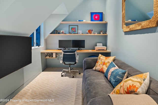 office space featuring built in shelves, built in desk, light colored carpet, and vaulted ceiling