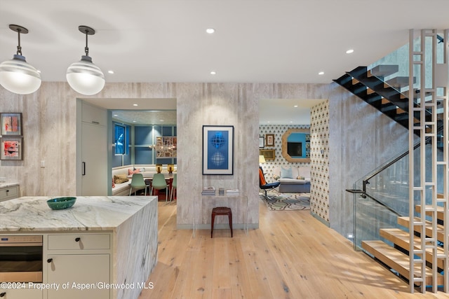 kitchen featuring light stone countertops, wall oven, pendant lighting, light hardwood / wood-style flooring, and white cabinets