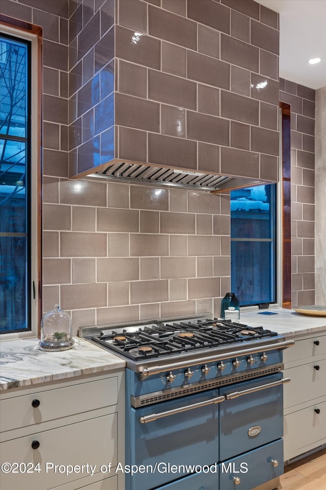 kitchen with white cabinets, light stone counters, stainless steel stove, and tasteful backsplash