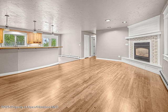 885 Stout St, Craig, CO 81625 - unfurnished living room featuring light wood-style flooring, baseboard heating, a textured ceiling, baseboards, and a brick fireplace