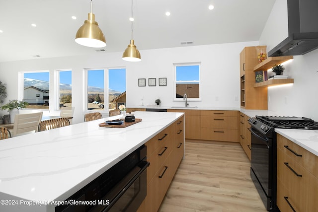 kitchen featuring light stone countertops, wall chimney exhaust hood, black range with gas stovetop, pendant lighting, and light hardwood / wood-style floors